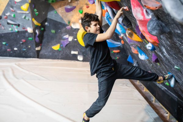 Jugendlicher klettert an einer Boulderwand in einer Kletterhalle mit bunten Griffen.